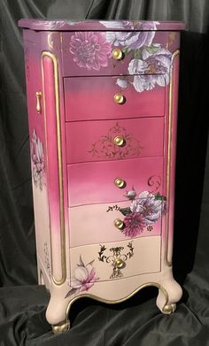 a pink and gold dresser with flowers painted on it's sides, sitting on a black background