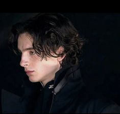 a young man with curly hair wearing a black jacket and looking off into the distance