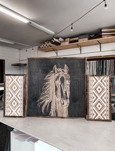 three framed art pieces on a table in front of a blackboard with a drawing of a horse