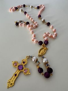 This is a beautiful gold chain link Rosary made with pretty pink and purple glass beads and white Pearl beads.  The white Pearl beads are accented with gold caps and surrounded with small amethyst beads.  Attached is a 2" gold crucifix with some added purple and pink gem embellishments.  The Virgin Mary Miraculous Medal finishes off this gorgeous Rosary.   The Rosary consists of 10 mm Our Father beads and 8 mm Hail Mary beads.  Length of the Rosary is approximately 22 1/2". This Rosary is handma Gold Amethyst Jewelry With 8mm Beads, Purple Beaded Rosary As Gift, Beaded Amethyst Gold Jewelry, Gold Amethyst Beaded Necklace With Faceted Beads, Pink Beaded Amethyst Necklace, Purple Pearl Jewelry With Colorful Beads, Gold Caps, Pink Gem, The Virgin Mary