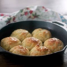 some biscuits are in a black pan on a wooden table next to a flowered cloth