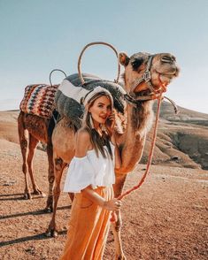 a woman standing next to a camel in the desert