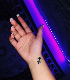 a woman's hand with a small cross tattoo on her left wrist and purple light in the background