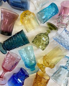 many different colored glass vases on a white tablecloth, all lined up together