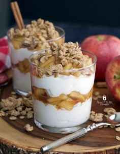 two glasses filled with dessert sitting on top of a wooden table next to an apple