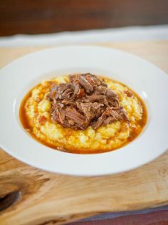 a white plate topped with meat and grits covered in gravy on top of mashed potatoes