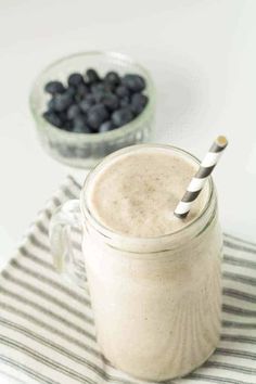 a smoothie in a mason jar with a striped straw and blueberries next to it