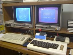 two old computers sitting on top of a wooden desk in front of a computer monitor