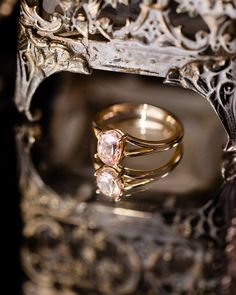 two wedding rings sitting on top of each other in front of an ornate frame and mirror