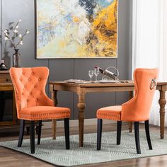 two orange chairs sitting at a table in front of a painting