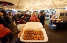 a person holding up a tray with donuts in front of people at an outdoor market