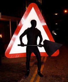 a man holding an umbrella standing in front of a road sign at night with his back turned to the camera