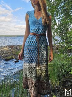 a woman is standing by the water wearing a blue and white crochet dress