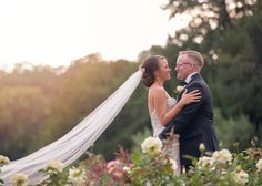 a bride and groom standing in the middle of flowers with their arms around each other