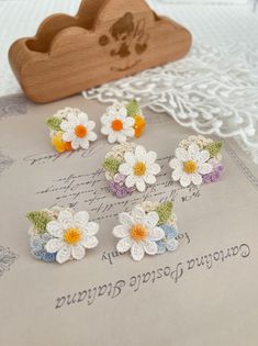 several crocheted flowers are sitting on top of an open book with a wooden heart in the background