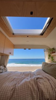 a bed sitting under a skylight in a bedroom next to the ocean and beach