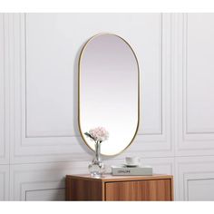 a mirror sitting on top of a wooden dresser next to a vase with flowers in it