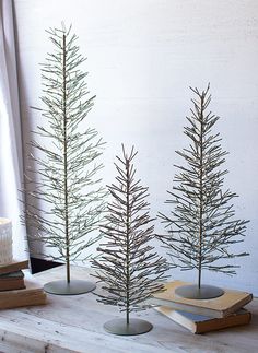 three small pine trees sitting on top of a table next to books and a candle