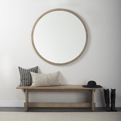 a wooden bench sitting under a round mirror next to a black boot and white wall