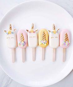 four unicorn - shaped pops are on a white plate with gold and pink decorations,