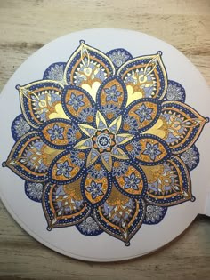 an intricate blue and gold flower design on a white round surface with a wooden table in the background