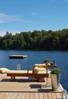 a wooden dock with two chaise lounges on it's sides and trees in the background