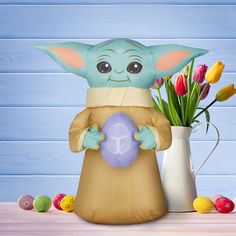 an inflatable baby yoda holding a purple ball next to some tulips