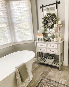 a white bath tub sitting under a window next to a sink in a room with wooden floors