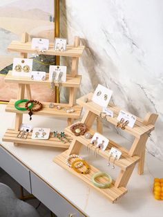 three wooden shelves with jewelry on them in front of a mirror and other items sitting on the counter