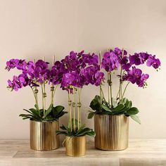 three gold vases with purple flowers in them