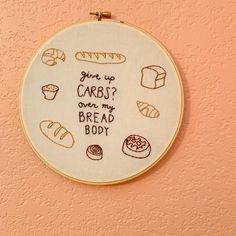 a cross stitch hoop hanging on the wall with some bread and cupcakes written in it