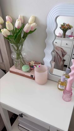 a white table topped with a vase filled with pink tulips next to a mirror