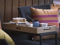 a tray with some food on it sitting next to a chair and pillows in front of a wooden wall