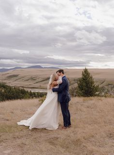 a bride and groom kissing on top of a hill