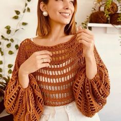 a woman wearing a brown crochet top and white pants is smiling at the camera