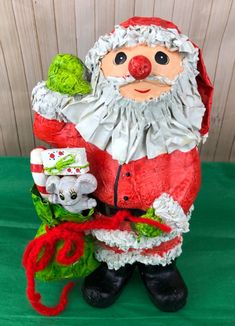 a santa clause figurine holding presents on a green surface