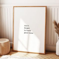 a white framed poster sitting on top of a wooden floor next to a vase filled with dry grass