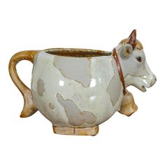 a ceramic cow mug with brown spots on it's body and horns sticking out of the cup