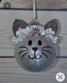 a cat ornament hanging on a wooden wall with flowers in it's hair