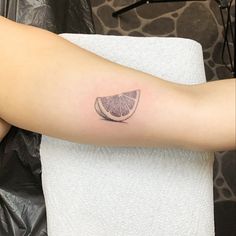 a woman's arm with a slice of grapefruit tattoo on her left arm