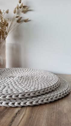 two round rugs sitting on top of a wooden table next to a vase with dried flowers