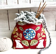 a red bag sitting on top of a white table next to a ball of yarn