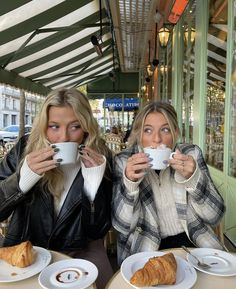 two women sitting at a table drinking coffee and croissants