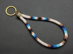 a blue, white and brown beaded keychain on a black surface with a gold metal hook