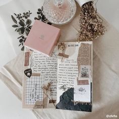 an open book sitting on top of a bed next to a vase with flowers and other items