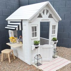 a small white house sitting on top of a gravel ground next to a wooden table