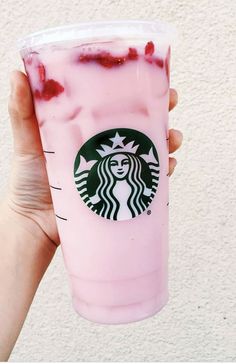 someone holding up a pink starbucks drink with strawberries on it