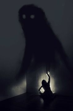 a person kneeling down in front of a wall with the shadow of a creepy creature on it