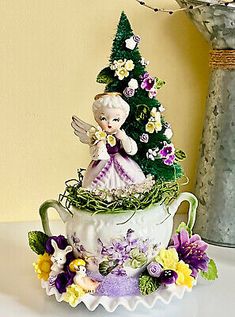 a tea cup with a fairy figurine sitting on top of it next to a vase