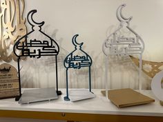 three metal sculptures sitting on top of a white table next to a plaque with arabic writing